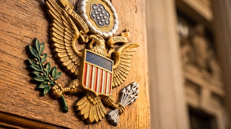 A detailed close-up of the Great Seal of the United States showing the bald eagle holding a ribbon with the motto E Pluribus Unum in its beak, with an olive branch in one talon and arrows in the other